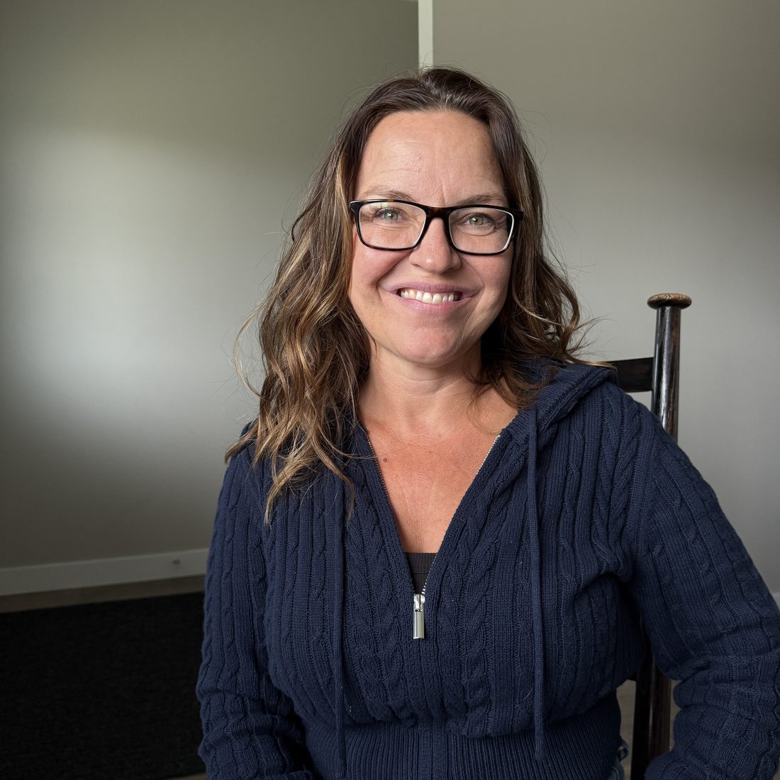 Tina Ross, smiling, seated in a wooden chair